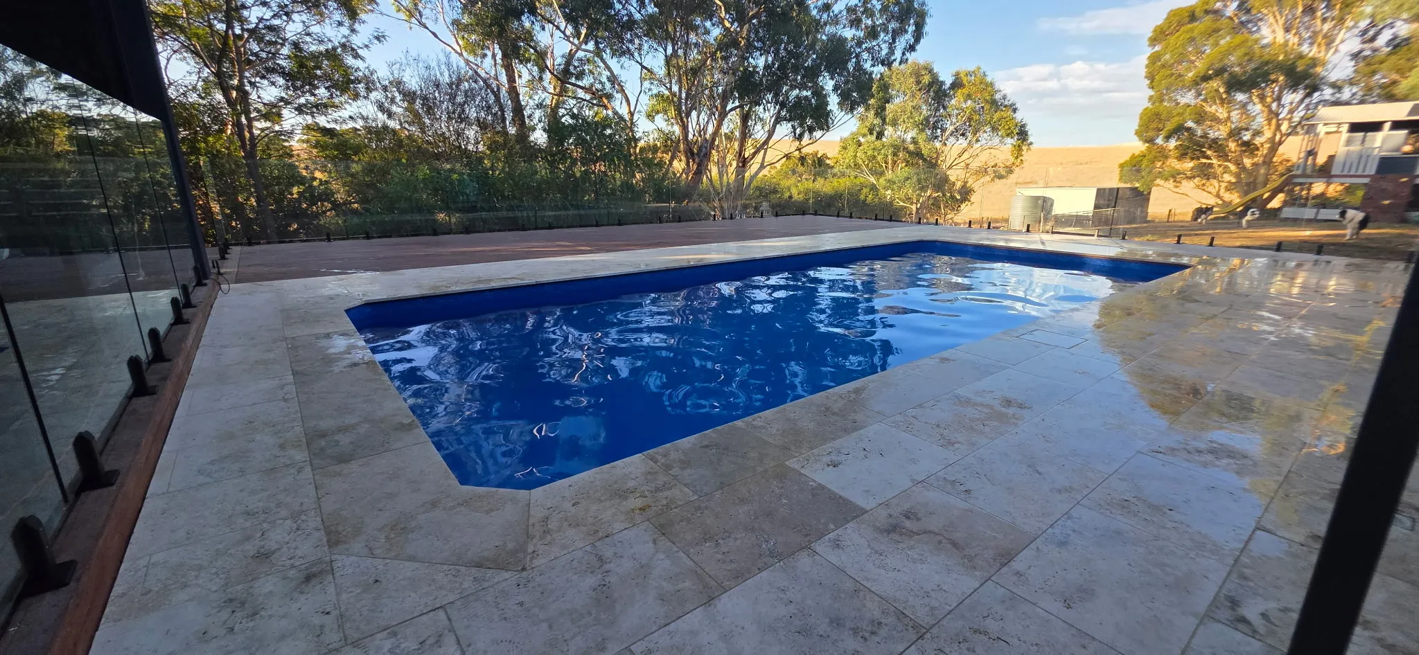 Renovated 9m x 4m hybrid pool at Mosquito Hill viewed from the entry end with travertine paving, frameless glass fencing, and native bushland backdrop
