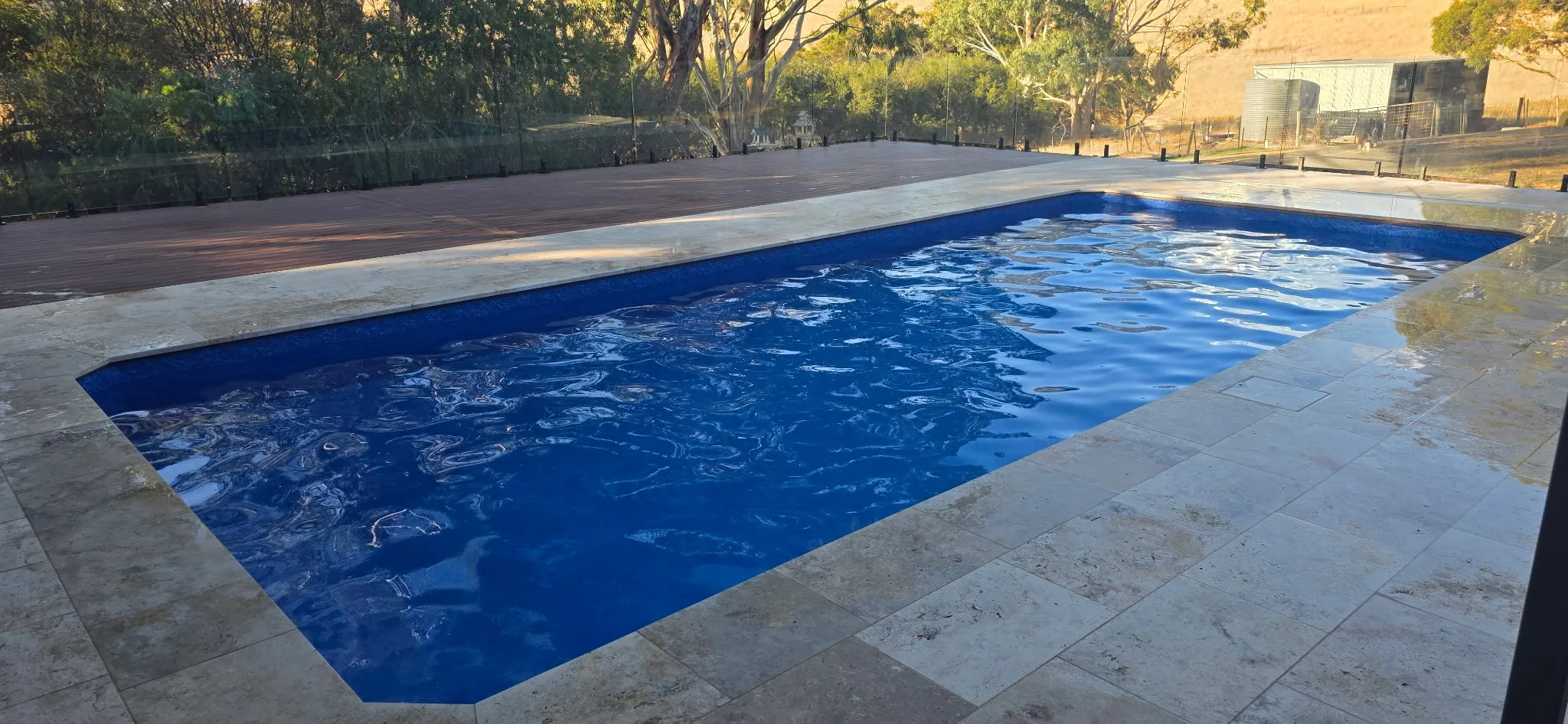 Deep end view of renovated Mosquito Hill pool showing Aqualux Maui liner, travertine surround, timber decking, and South Australian hills beyond