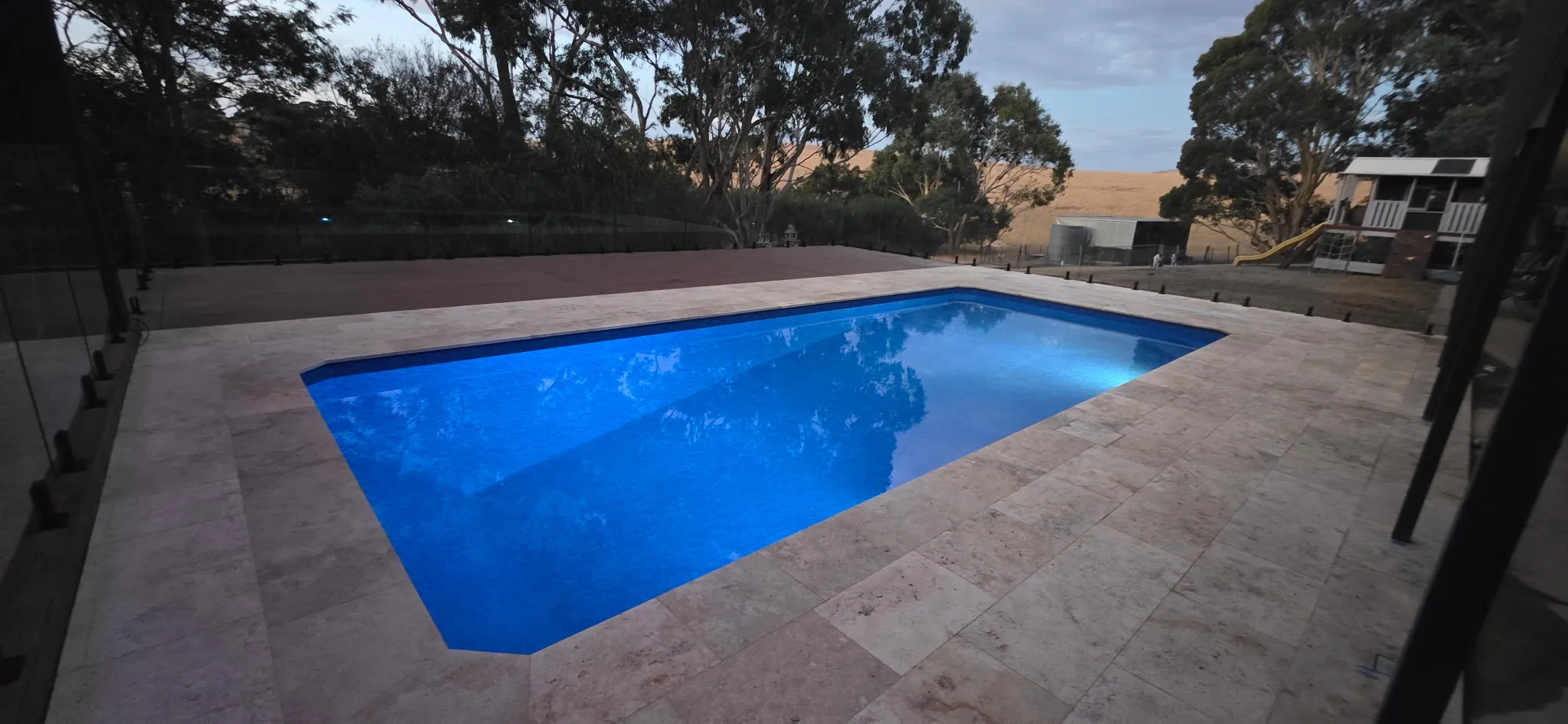Dusk view of Mosquito Hill pool with LED pool lights glowing blue against the fading sky and surrounding landscape