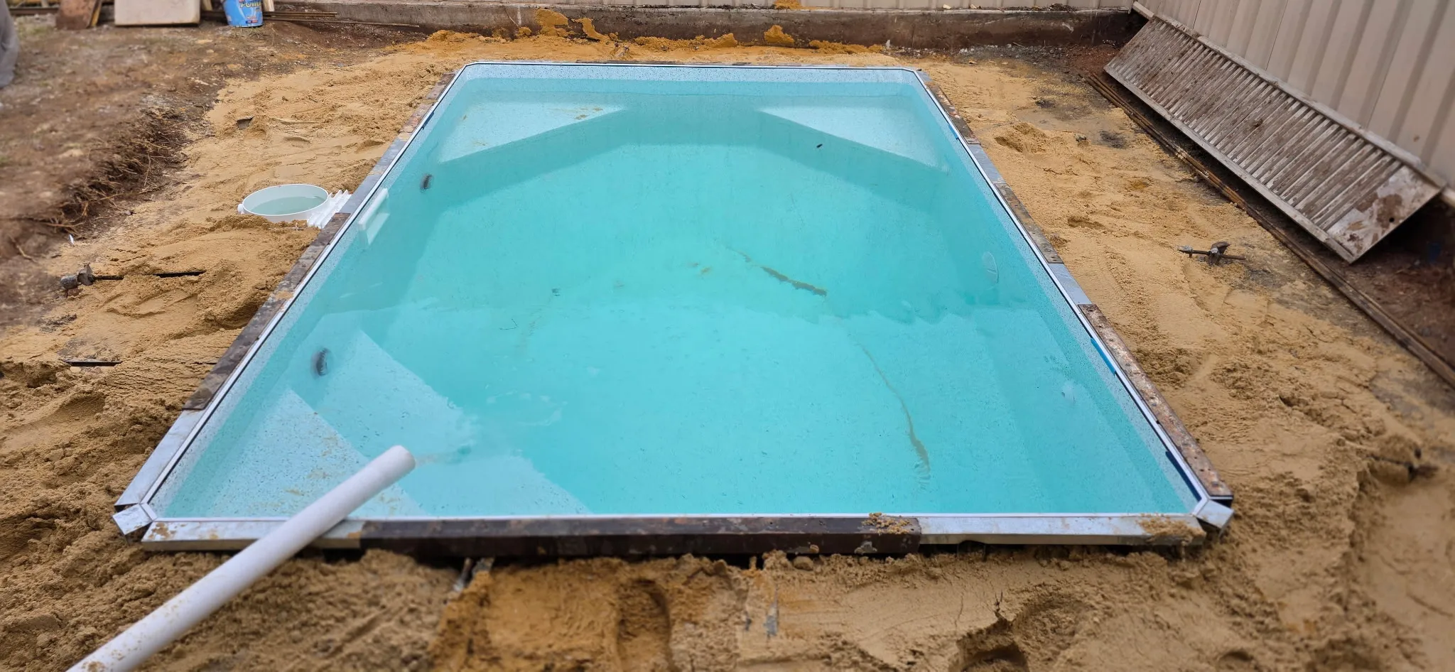 Plunge pool filling with water after liner install with sand backfill packed around pool walls