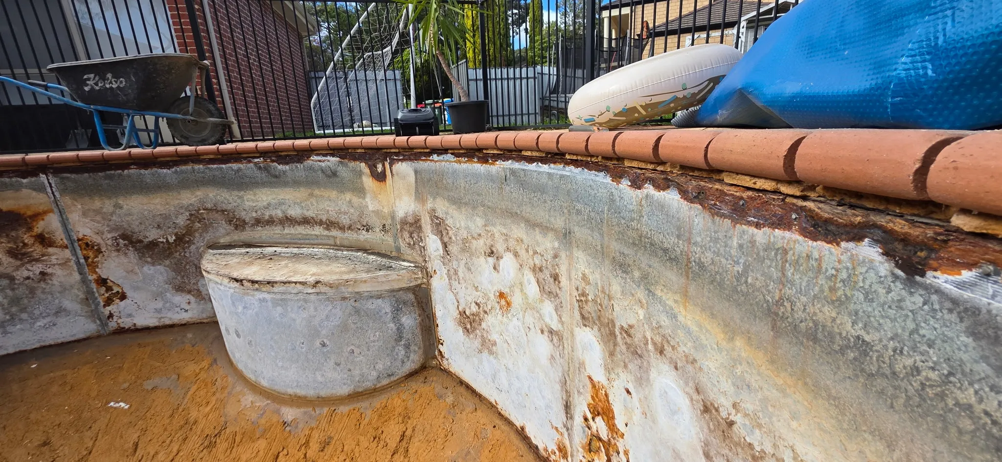 Close-up of corroded steel panels and deteriorated coping on kidney-shaped pool before renovation at Coromandel Valley