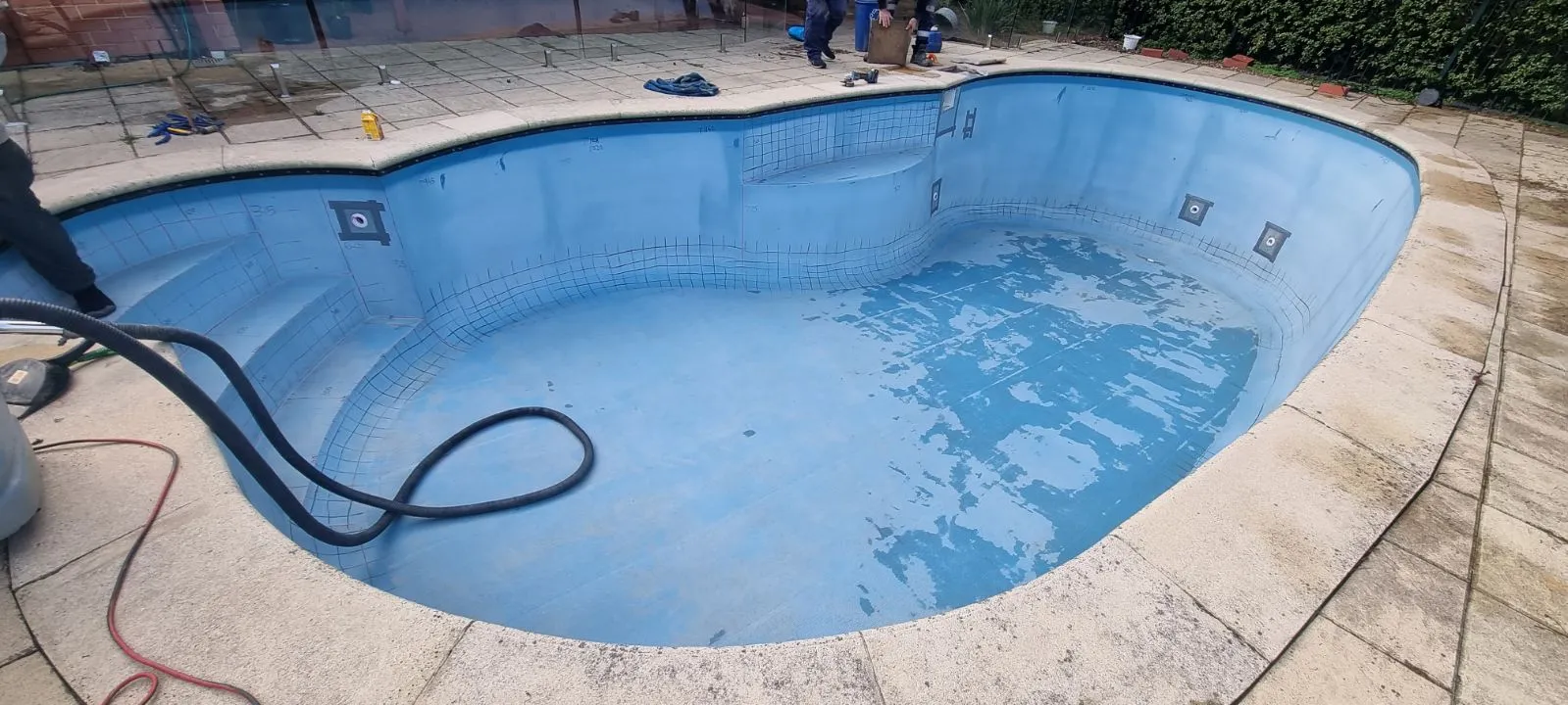 Wide angle of kidney-shaped fibreglass pool before renovation at Crafers showing deteriorated surface, step entry, and existing paving