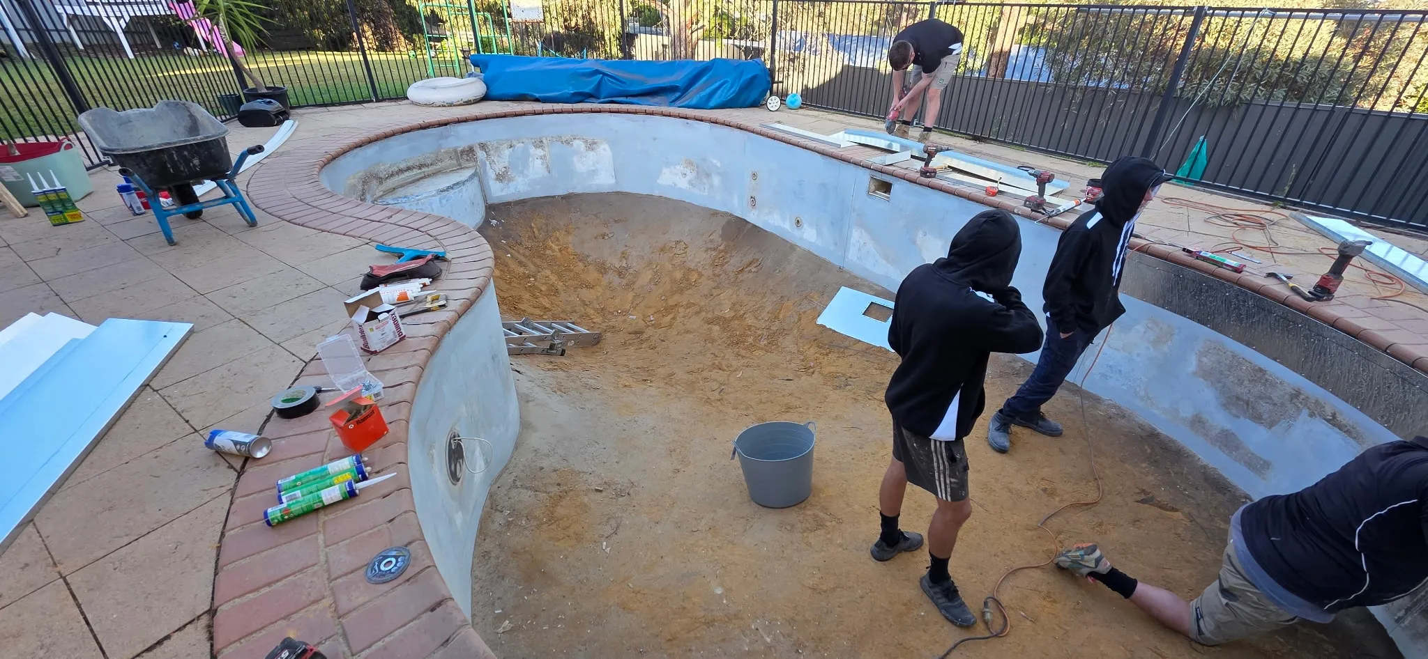 Adelaide Hybrid Pools team preparing the pool shell for liner installation with tools and materials around the kidney-shaped pool