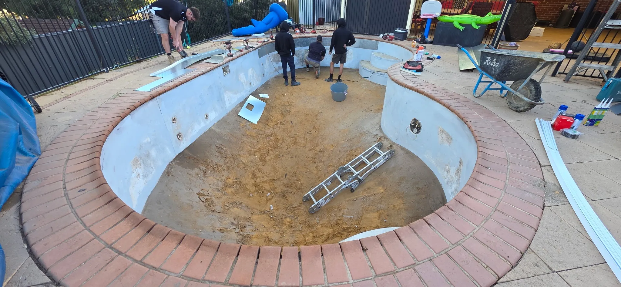 Wide angle of kidney-shaped pool shell during renovation prep showing repaired steel panels and bowled deep end