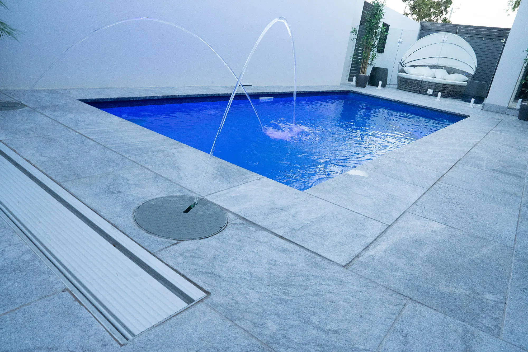 Close-up of twin laminar jets and large-format silver travertine paving showing precision joints and recessed jet installation
