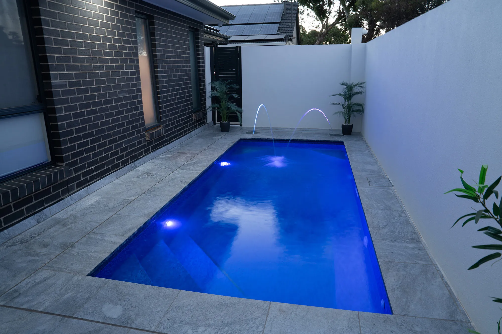 Dusk view of Largs North plunge pool with LED pool lights and laminar jets active against the rendered courtyard wall