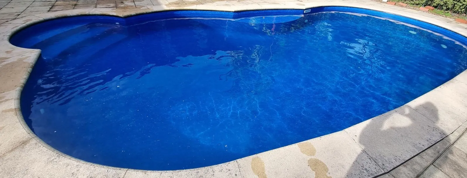 Wide angle of finished pool renovation at Crafers with vibrant blue vinyl liner in kidney shape and existing concrete paving