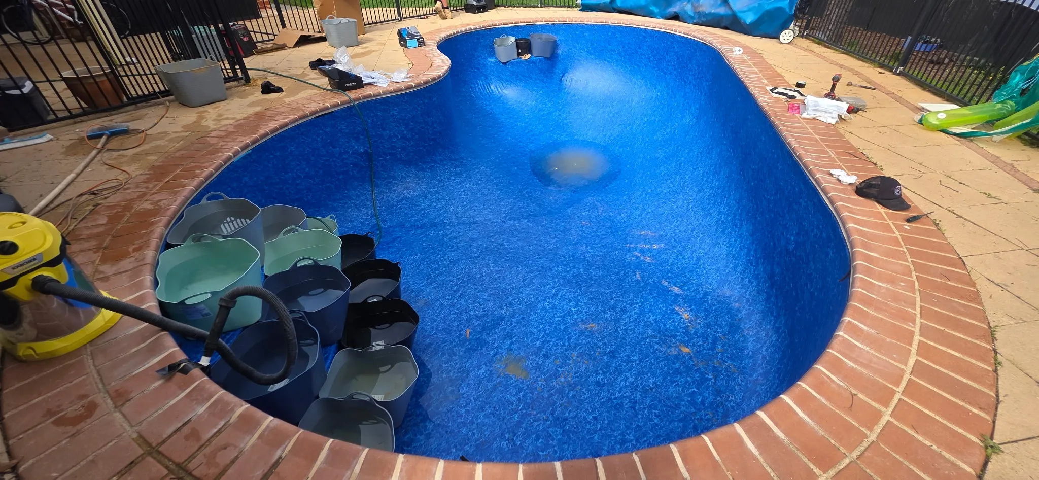 New Aqualux Maui vinyl liner installed in kidney-shaped pool with water filling in progress and buckets weighing liner