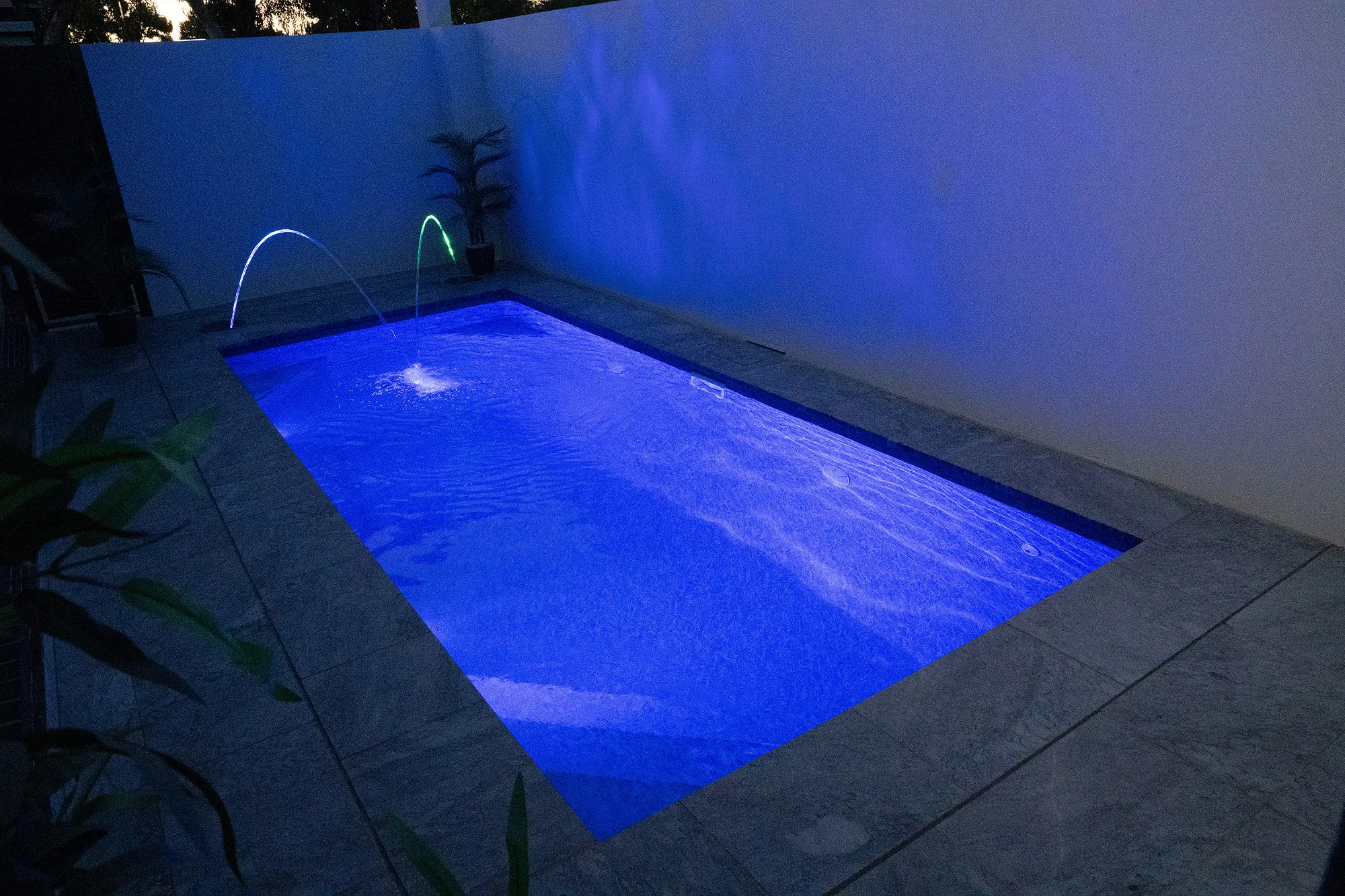 Night view of plunge pool with vivid blue LED lighting and twin laminar jets arcing across the water
