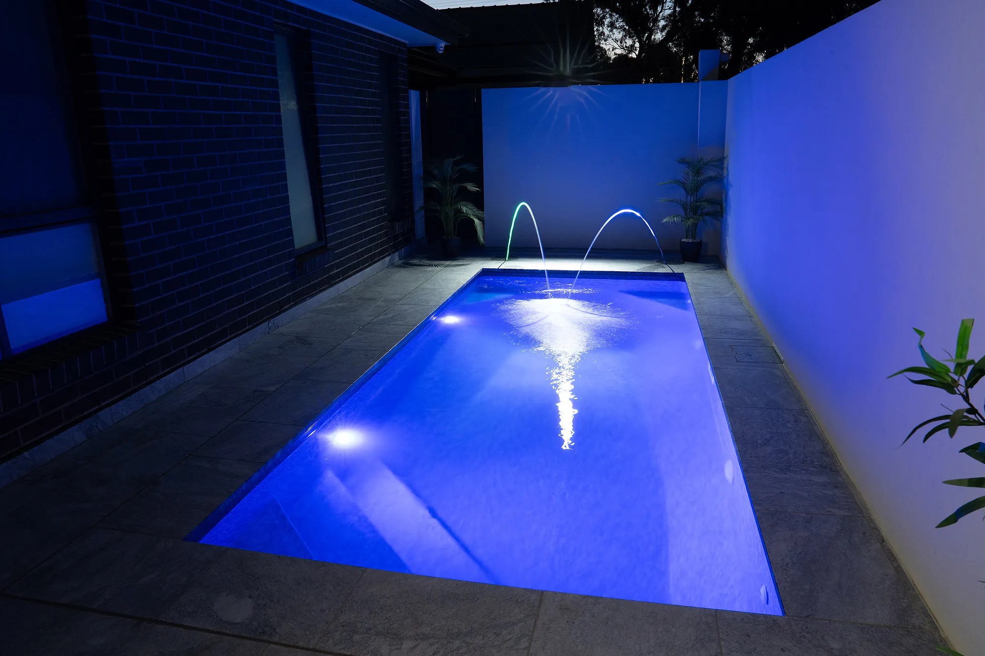 Night shot of Bayside Modern plunge pool with overhead light star burst, LED pool lights, and laminar jets running