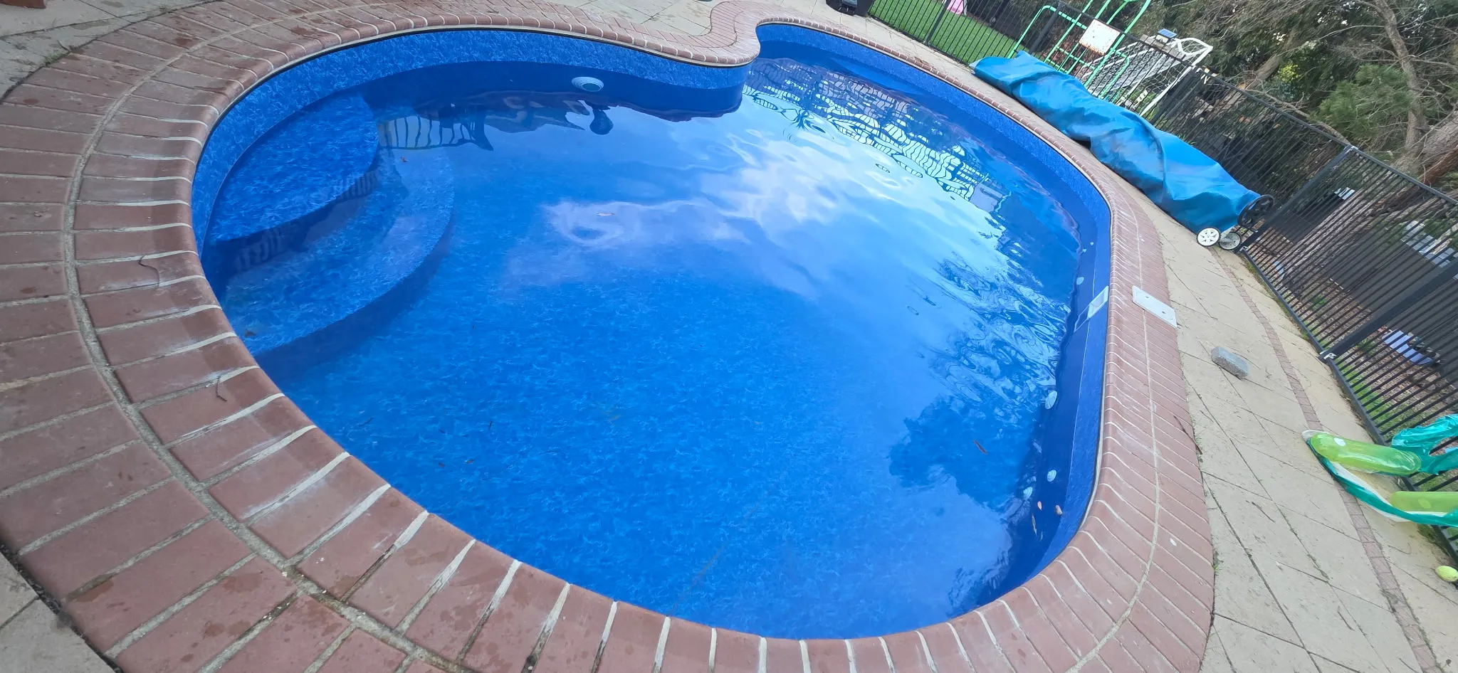 Entry end of finished pool renovation showing step entry, deep blue Maui liner, and repointed brick coping
