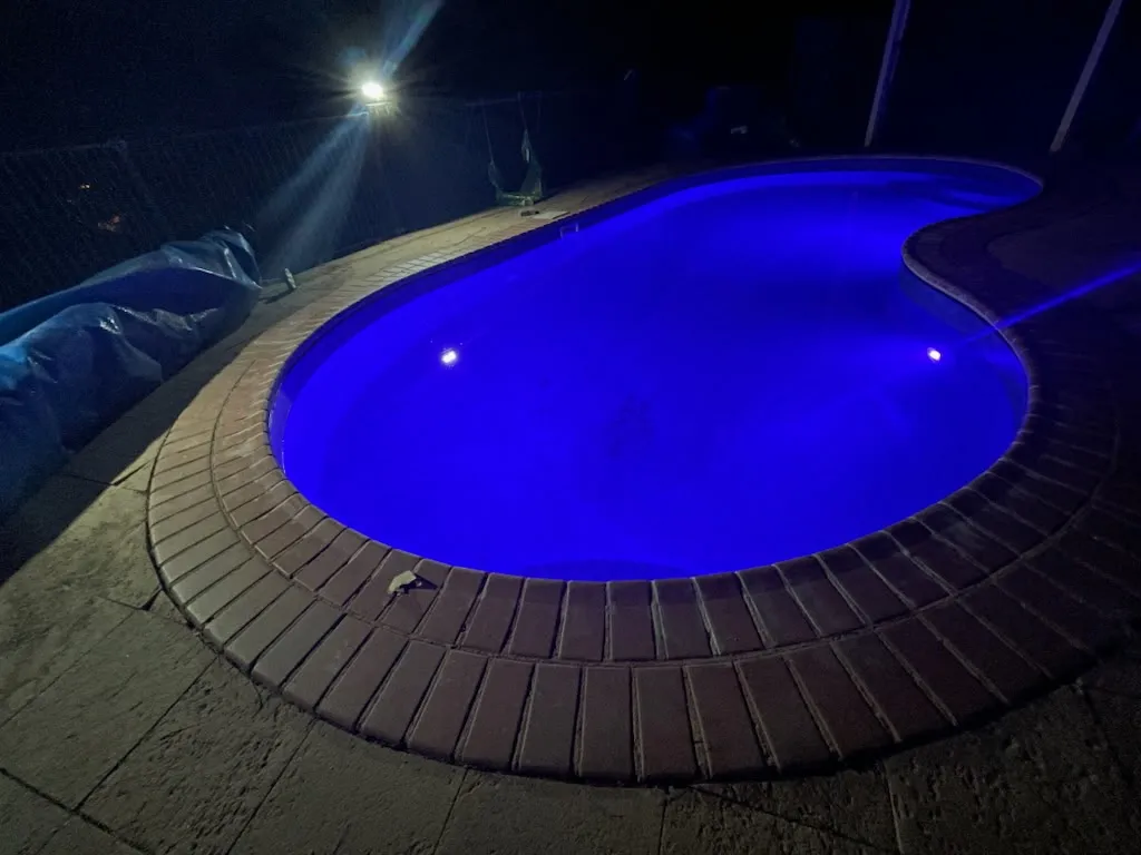 Night shot of renovated kidney-shaped pool with vivid blue LED lighting and brick coping at Coromandel Valley