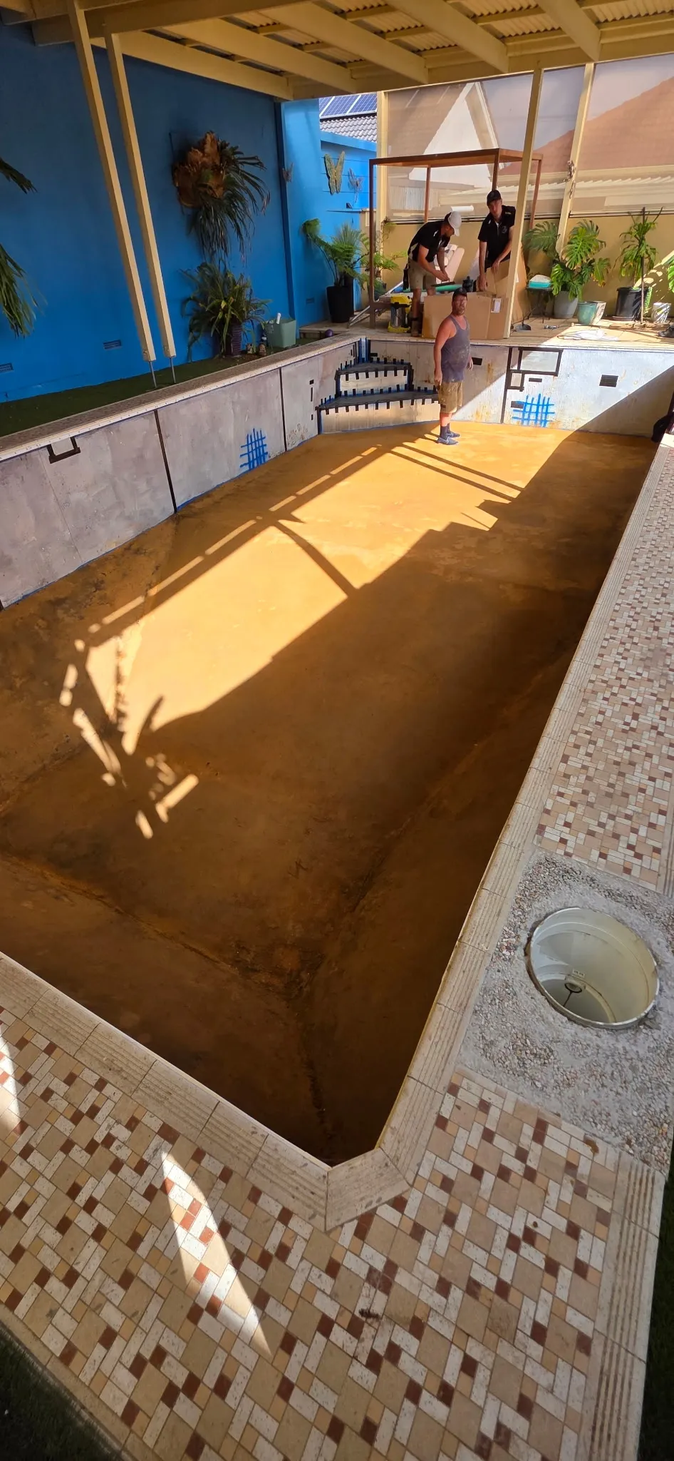 Adelaide Hybrid Pools team preparing pool shell for liner installation with tropical blue wall backdrop