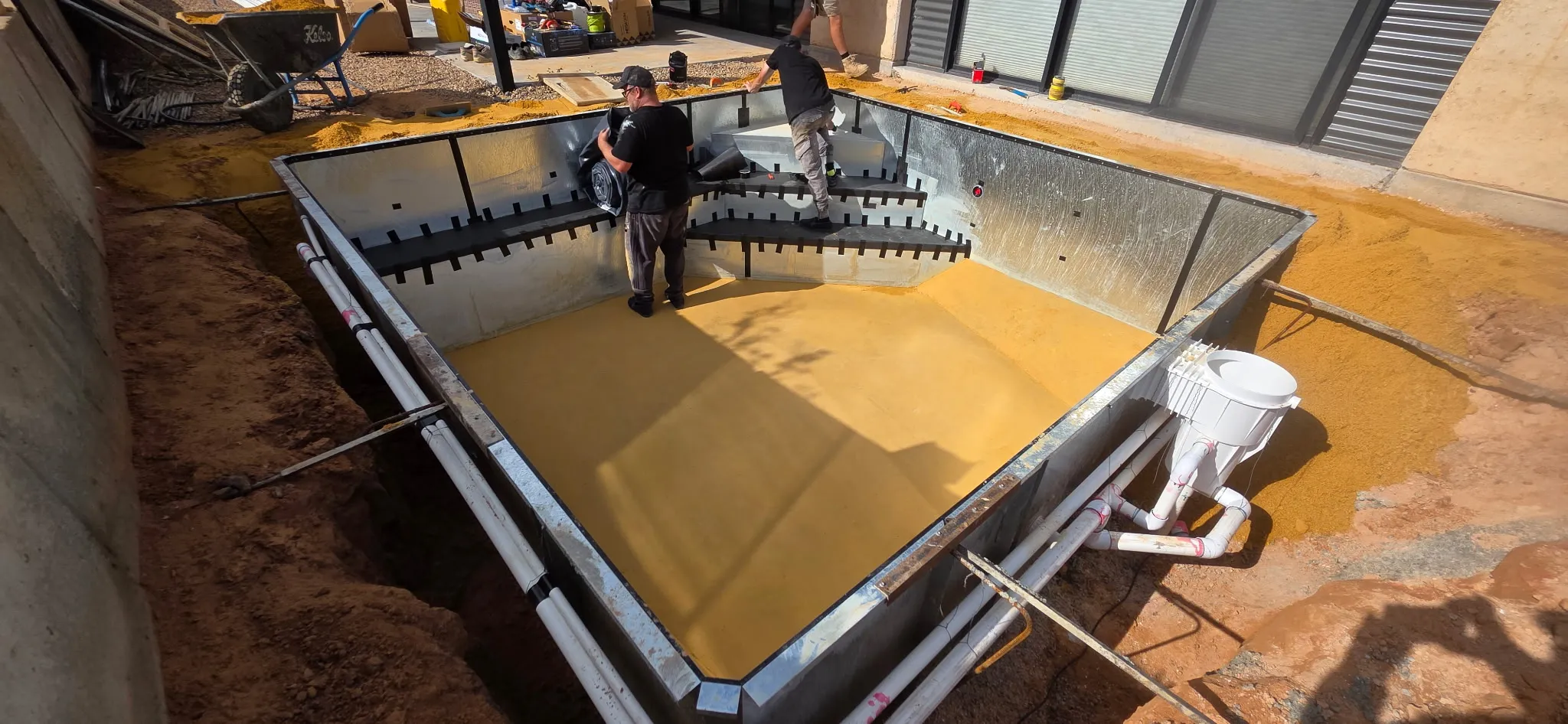 Team preparing sand base and rolling out Antique Black liner with plumbing runs visible