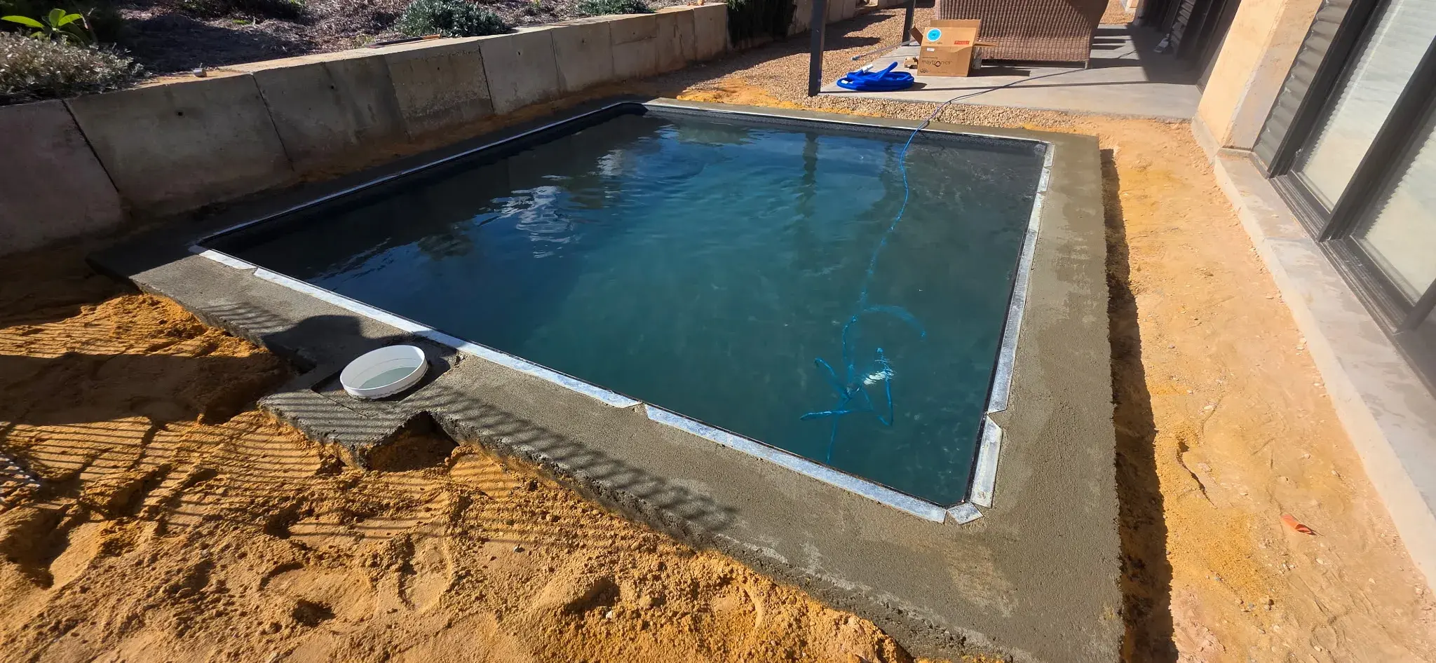 Filled pool showing dark Antique Black water tone against retaining wall and modern home