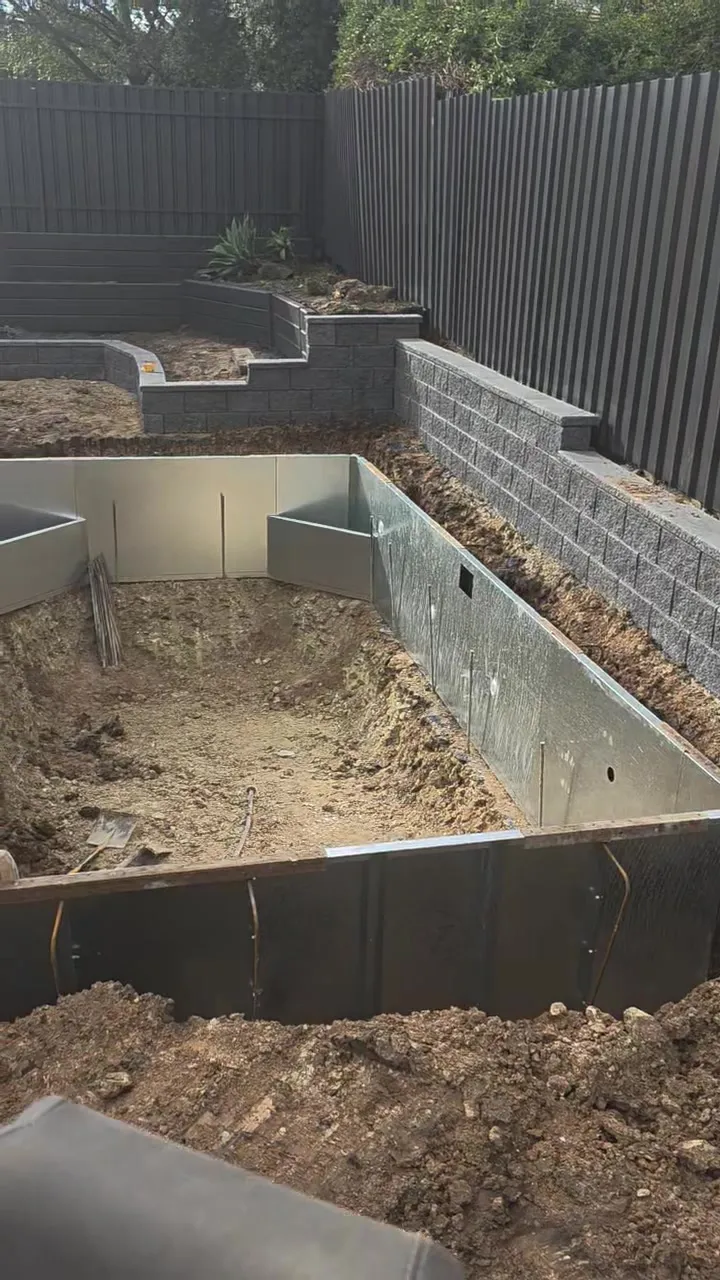 Steel wall panels of the hybrid pool shell installed at Woodcroft with block retaining wall behind